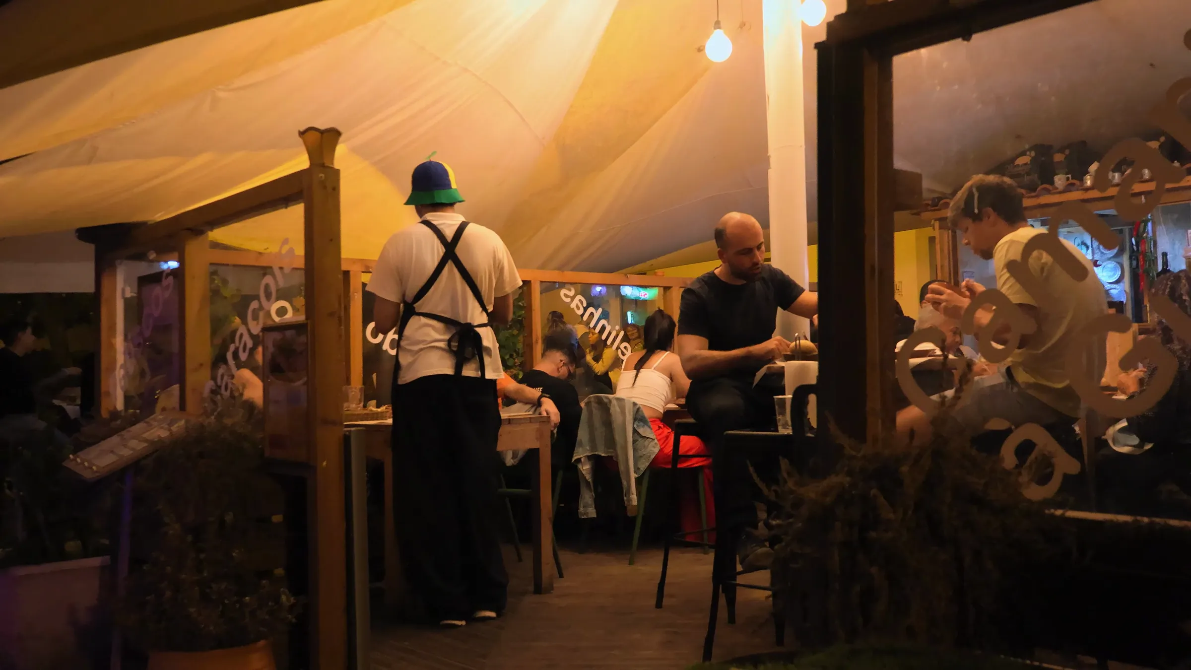 Esplanada coberta à noite, com clientes à mesa e um empregado de avental.